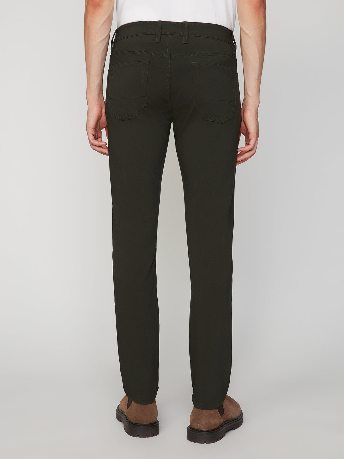A person is shown from the back wearing PROJEK RAW MENS 5-POCKET SOLID BUNGEE PANT in black with an elastic waistband, paired with a white shirt and brown shoes, standing against a plain light gray background.