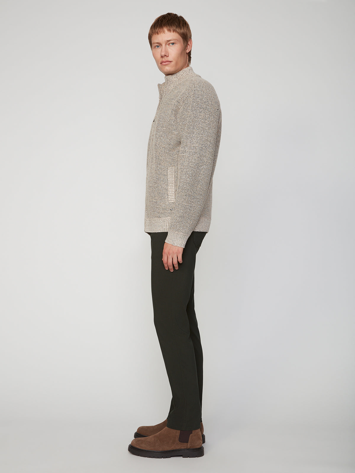 A person stands in profile against a plain background, wearing a light gray zip-up sweater, brown shoes, and PROJEK RAW MENS 5-POCKET SOLID BUNGEE PANT featuring an elastic waistband.