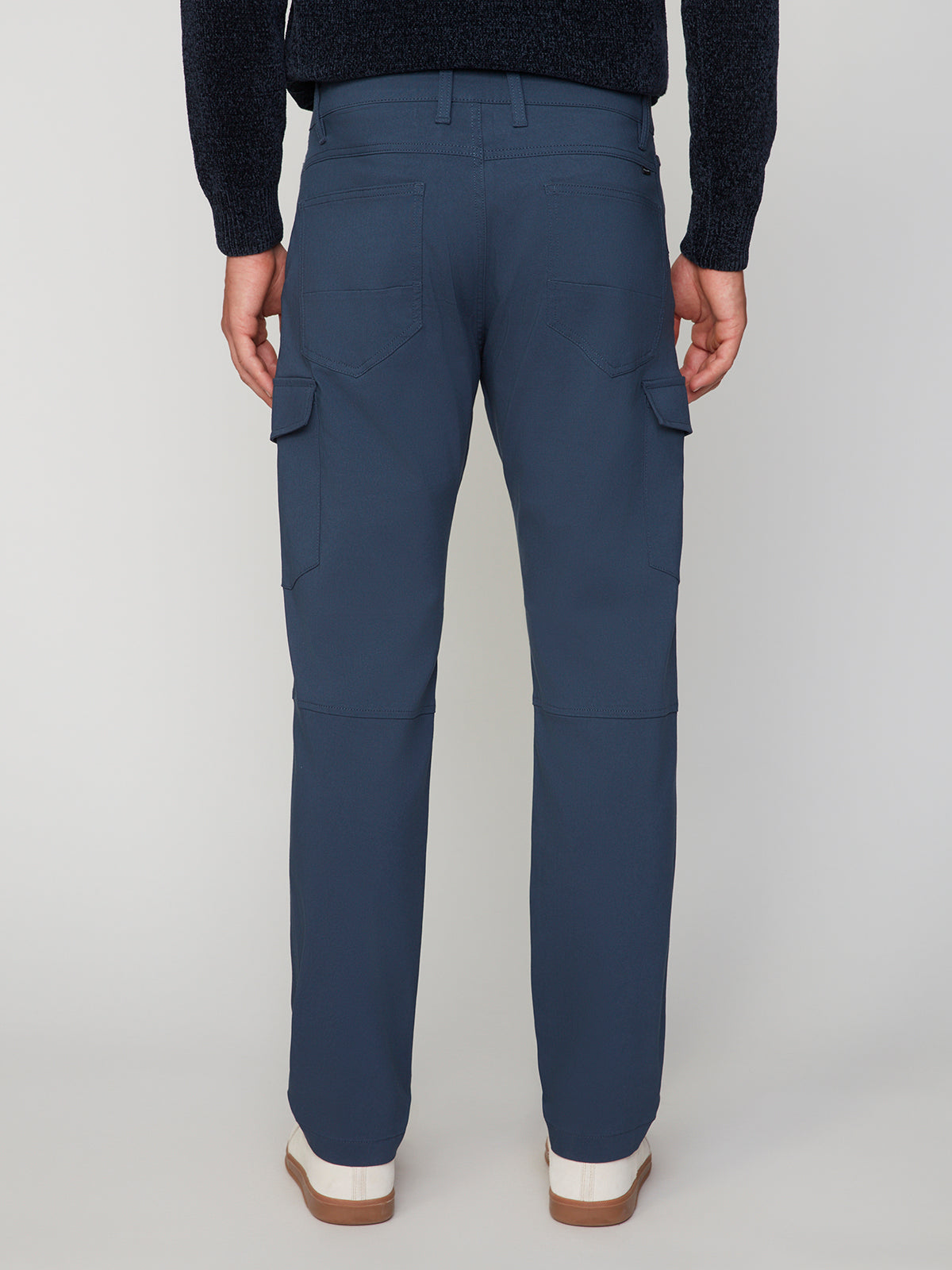 A person faces away from the camera, wearing PROJEK RAW MENS SOLID BUNGEE CARGO PANT with side pockets and a dark sweater. White shoes with brown soles complete the look against a plain, light background.