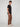 A man with curly brown hair models PROJEK RAW’s MENS SOLID BUNGEE CARGO PANT with an elasticized waistband, paired with a black t-shirt and white sneakers, standing sideways and looking at the camera against a plain background.