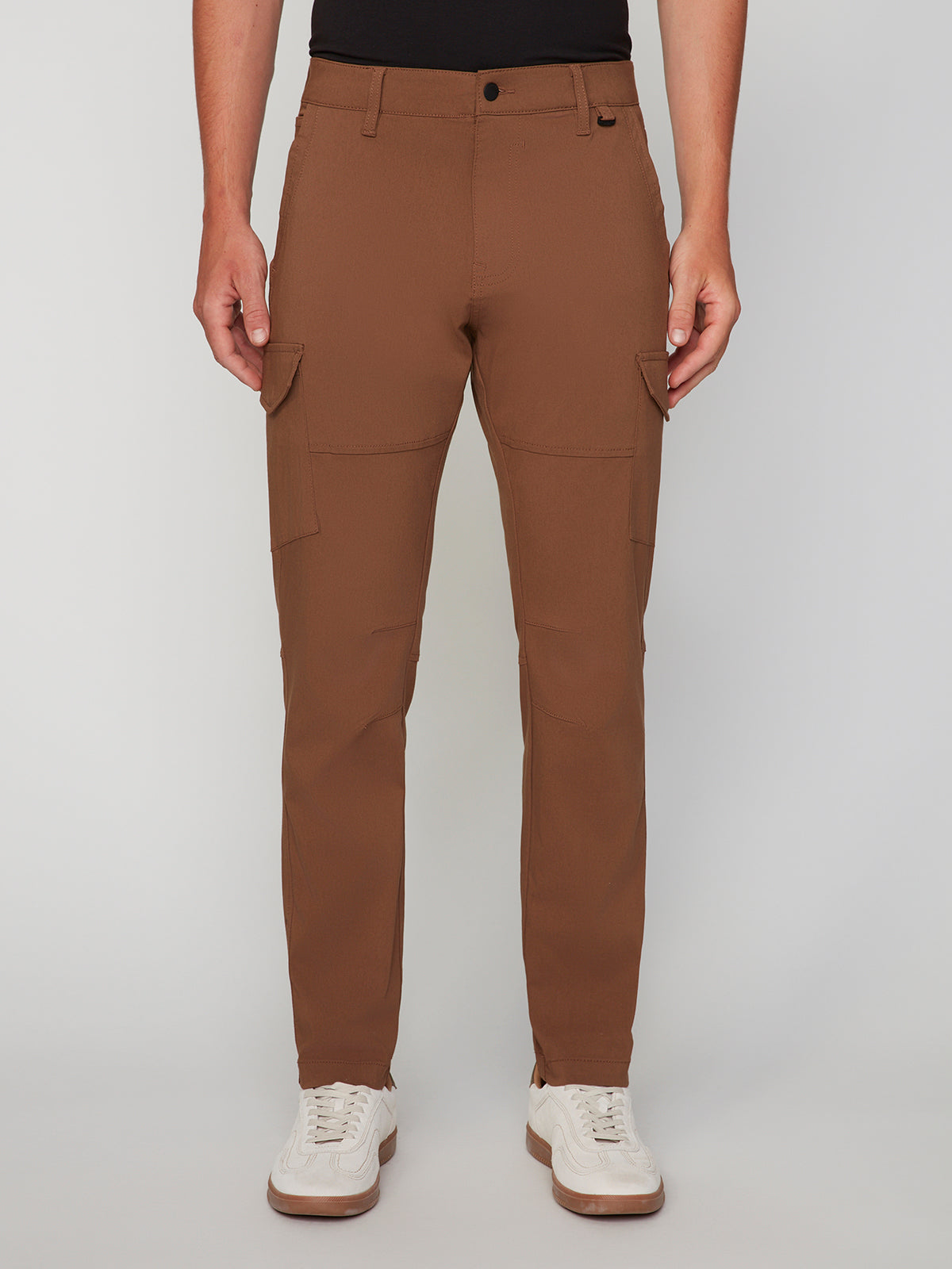 A person models the PROJEK RAW MENS SOLID BUNGEE CARGO PANT, featuring an elasticized waistband and side pockets, styled with a black top and white sneakers against a plain light background.