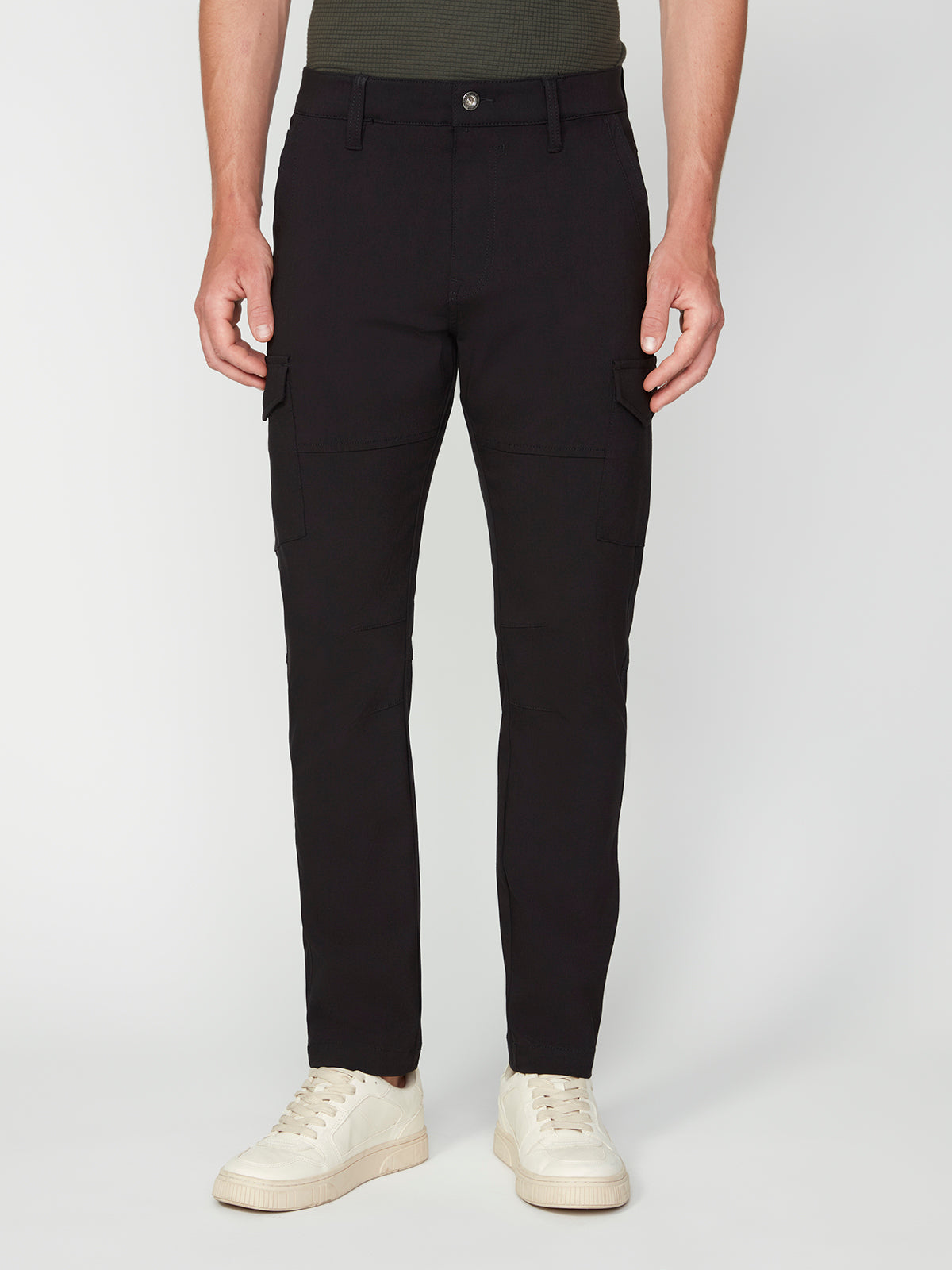A person wears PROJEK RAW MENS SOLID BUNGEE CARGO PANT streetwear in black, paired with white sneakers. The pants feature cargo and side pockets plus a secure button closure, all against a plain white background.