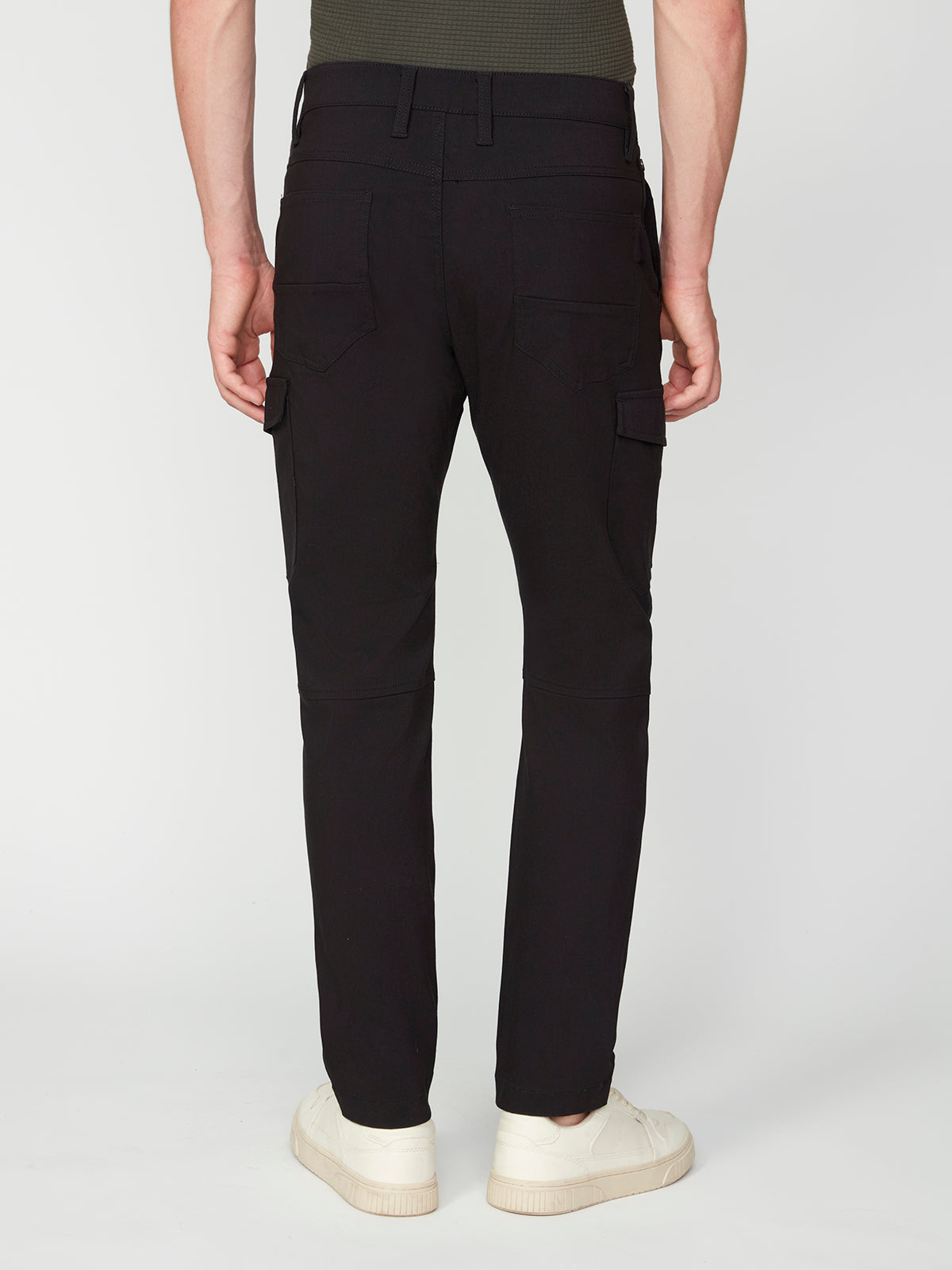 A person in PROJEK RAW MENS SOLID BUNGEE CARGO PANT with cargo pockets and white sneakers stands with their back to the camera against a white background, embodying modern streetwear style.