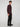 A man with curly brown hair stands in a studio, wearing a long-sleeve dark maroon shirt, PROJEK RAW MENS 5-POCKET SOLID BUNGEE CHINO PANT, and black shoes, facing slightly to the side against a plain light background.