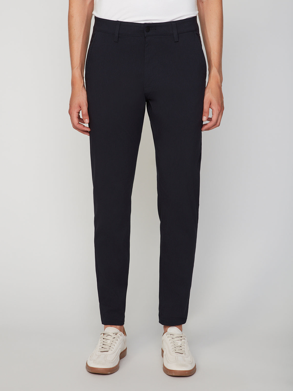 A person, shown from the waist down, wears PROJEK RAW MENS 5-POCKET SOLID BUNGEE CHINO PANT in dark navy and white sneakers, standing against a plain light background.
