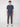 A young man with short curly hair stands against a white background, wearing a navy blue short-sleeve t-shirt, PROJEK RAW MENS SOLID BUNGEE FASHION CHINO PANT in a tailored fit, and white athletic sneakers.