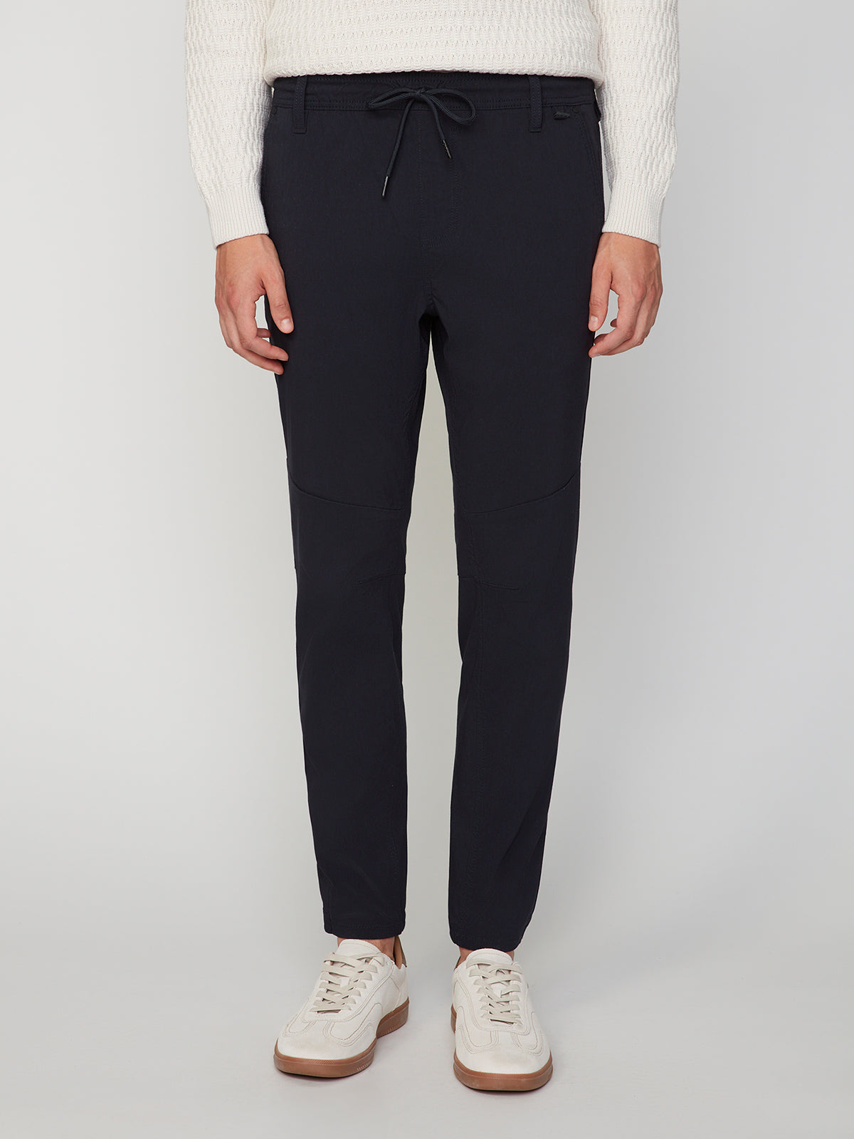 A person wearing PROJEK RAW MENS SOLID BUNGEE JOGGER in navy blue, styled with a white textured sweater and white sneakers, stands facing forward against a plain light background.