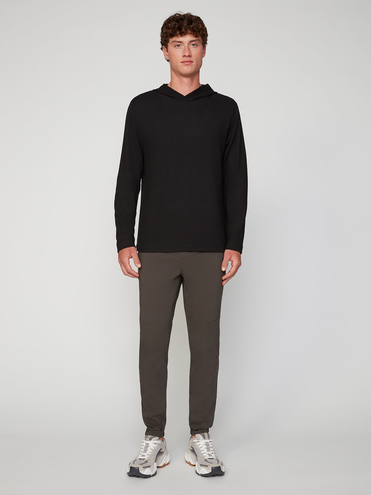 A young man faces forward against a plain light-gray background, wearing PROJEK RAW MENS SOLID BUNGEE JOGGER pants with an elastic waistband, a black long-sleeve hooded shirt, and white athletic sneakers.