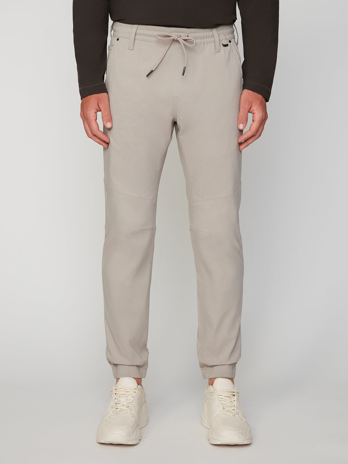 A person wearing PROJEK RAW MENS SOLID BUNGEE JOGGER with an elastic waistband, paired with a dark long-sleeve top and white sneakers, stands against a plain background.