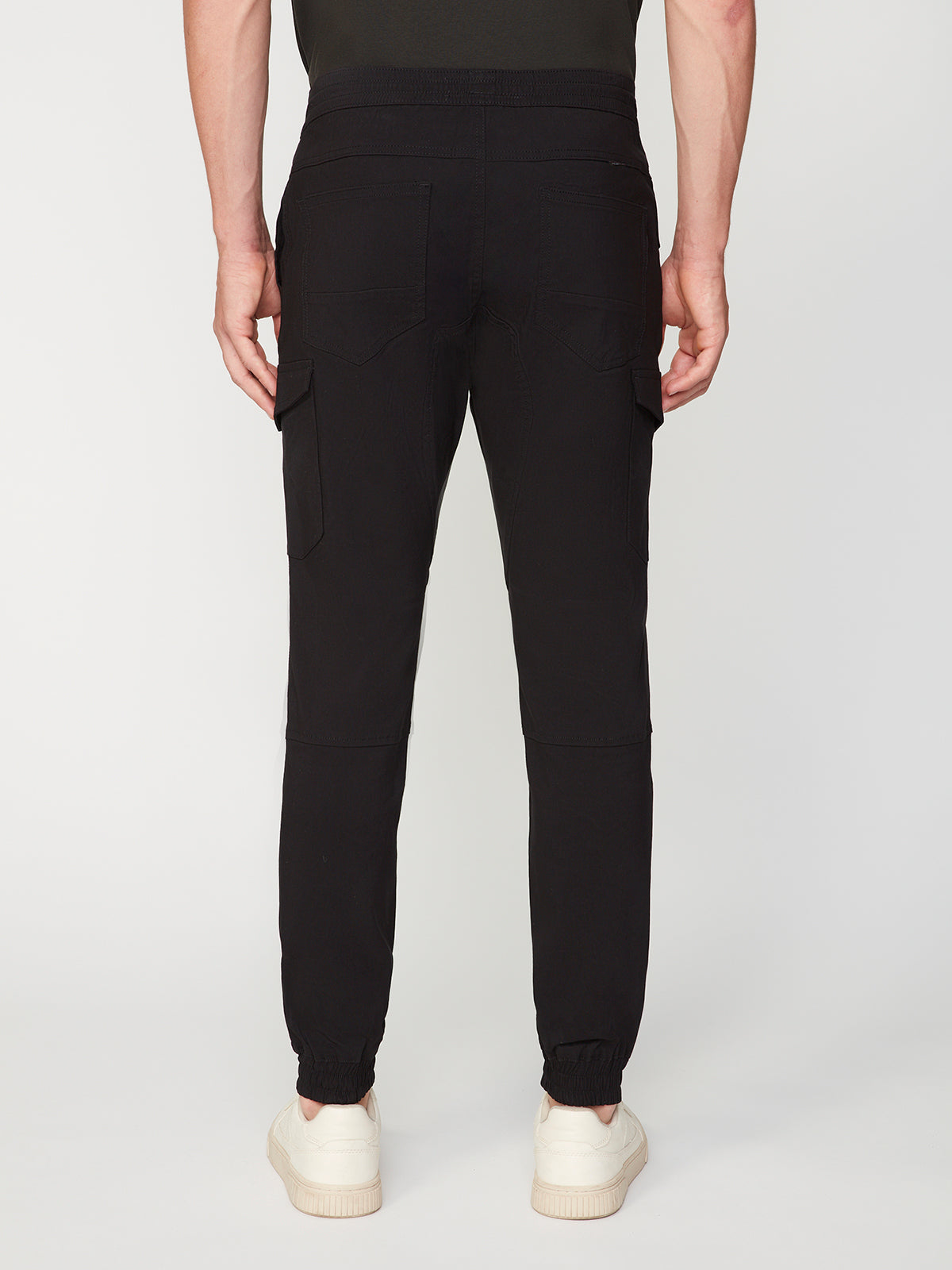 A person is shown from the back against a plain white background wearing PROJEK RAW MENS SOLID BUNGEE CARGO JOGGER with an elasticized waistband, cargo and side pockets, and elastic cuffs at the ankles, paired with white sneakers.