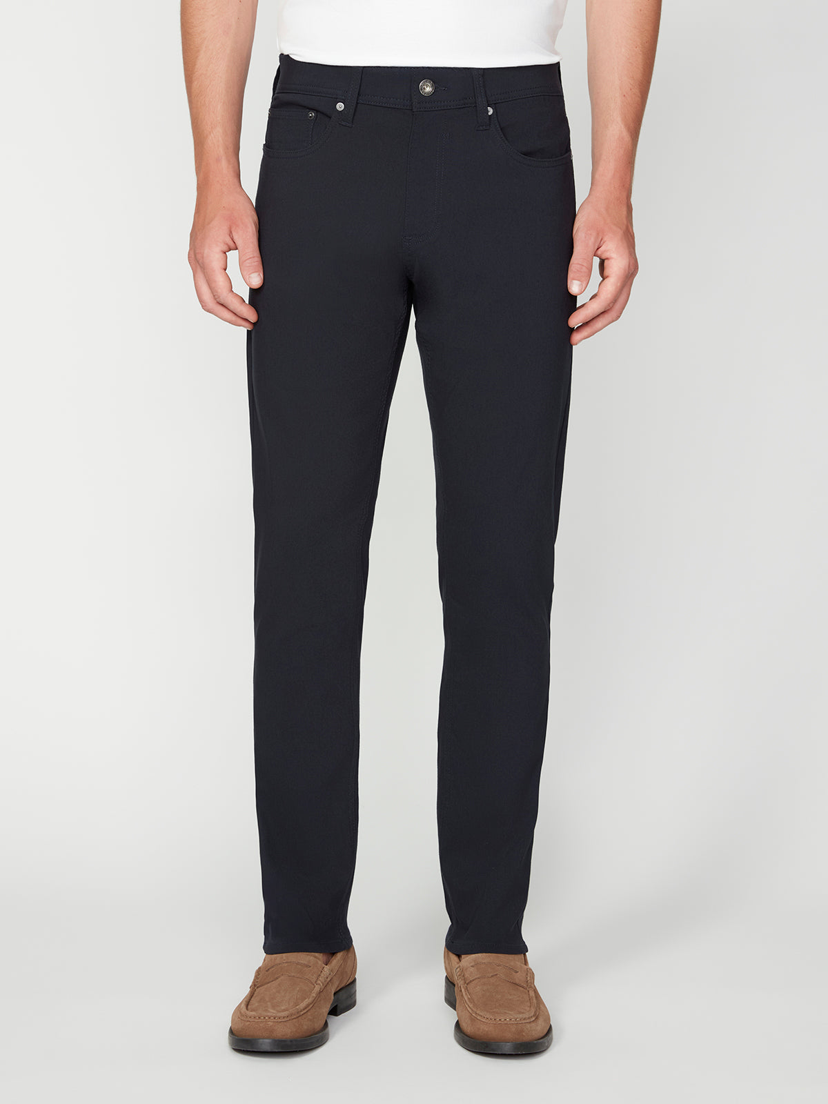 A person wears PROJEK RAW MENS SOLID BUNGEE RELAXED 5-POCKET PANT in black with brown suede loafers, standing against a plain white background. Their upper body is partially visible, revealing a crisp white shirt.