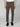 A person stands facing forward in PROJEK RAW MENS 5-POCKET BUNGEE TWILL PANT (brown), a white shirt, and black loafers. The image is cropped at the shoulders, focusing on the pants and shoes against a plain light backdrop.