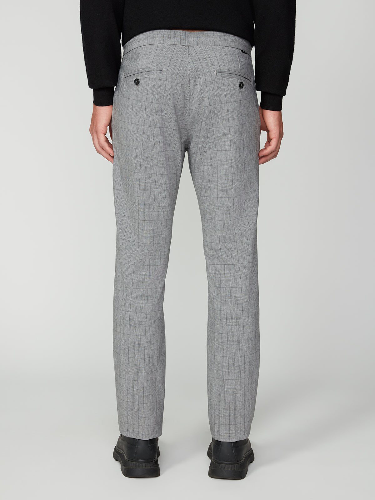 A person faces away, showcasing the back of PROJEK RAW MEN’S PLAID BUNGEE DRAWSTRING PANT in light gray, paired with a black sweater and black shoes.