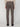 A person faces away wearing PROJEK RAW MENS SOLID BUNGEE RELAXED 5-POCKET PANT in brown with buttoned back pockets, a beige sweater, and black shoes. The pants have a tailored fit and the background is plain and light-colored.