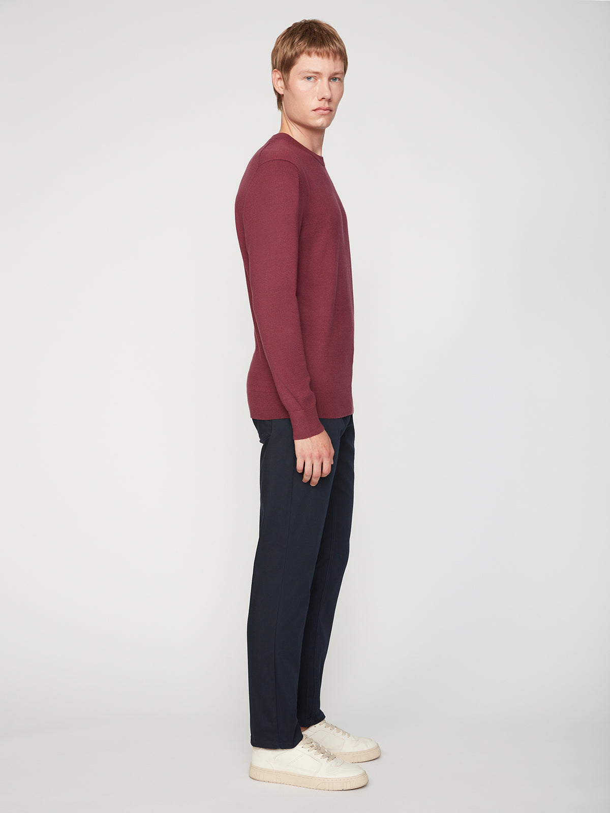 A young man stands in profile against a plain white background, wearing a long-sleeve maroon sweater, PROJEK RAW MENS CANVAS BUNGEE 5-POCKET PANT, and white sneakers.