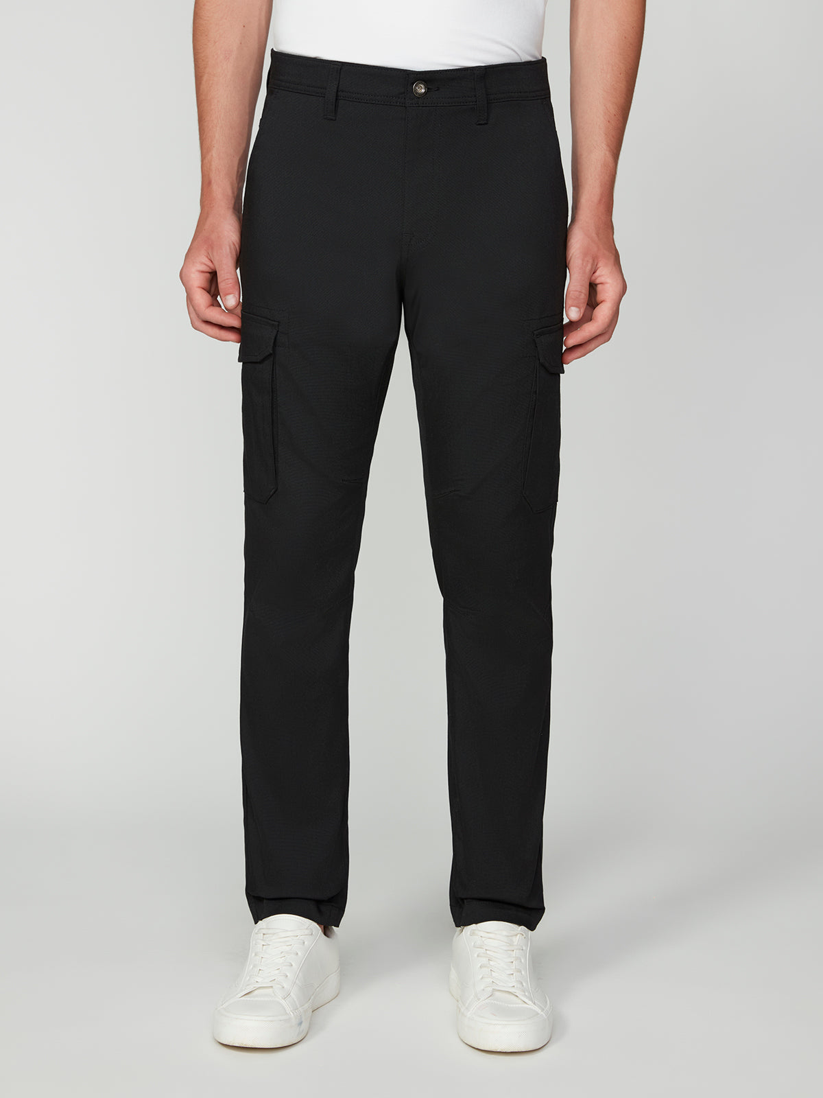 A person models PROJEK RAW MENS CANVAS BUNGEE RELAXED CARGO PANT, paired with white sneakers, standing forward against a plain light gray background. Only the lower half of the body is visible.