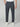 A person wearing PROJEK RAW MENS CANVAS BUNGEE RELAXED CARGO PANT in dark gray, paired with a white shirt and white sneakers, stands hands in pockets against a light gray background.