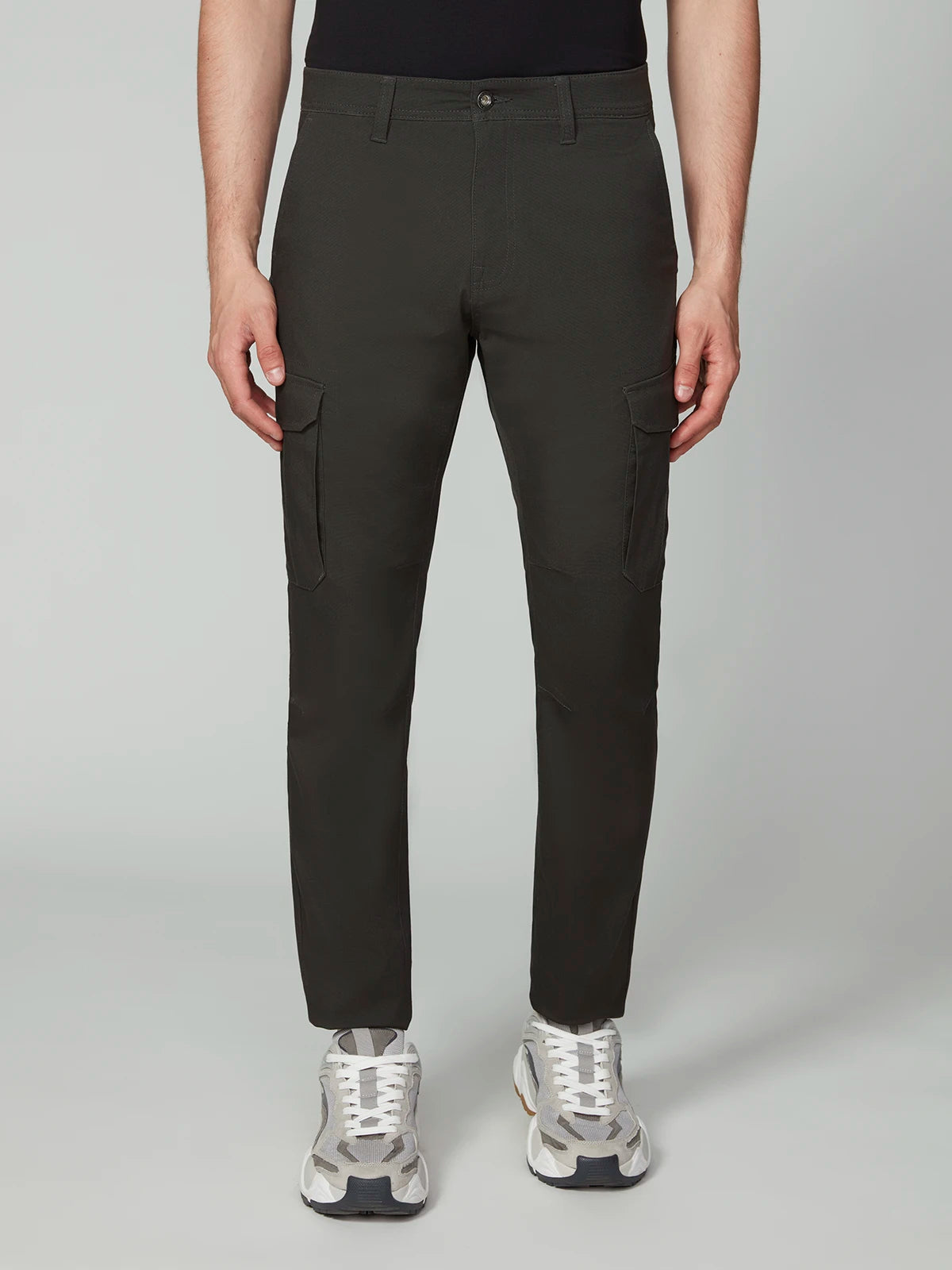 A person models PROJEK RAW MENS CANVAS BUNGEE RELAXED CARGO PANT in black, paired with white sneakers, facing forward against a plain light gray background. The photo is cropped at the shoulders to highlight the pants and shoes.