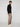 A young man stands sideways against a plain background, wearing a black zip-up sweater, PROJEK RAW MENS BARU5-POCKET STRAIGHT FIT DENIM PANT, and white sneakers. He looks slightly toward the camera with a neutral expression.