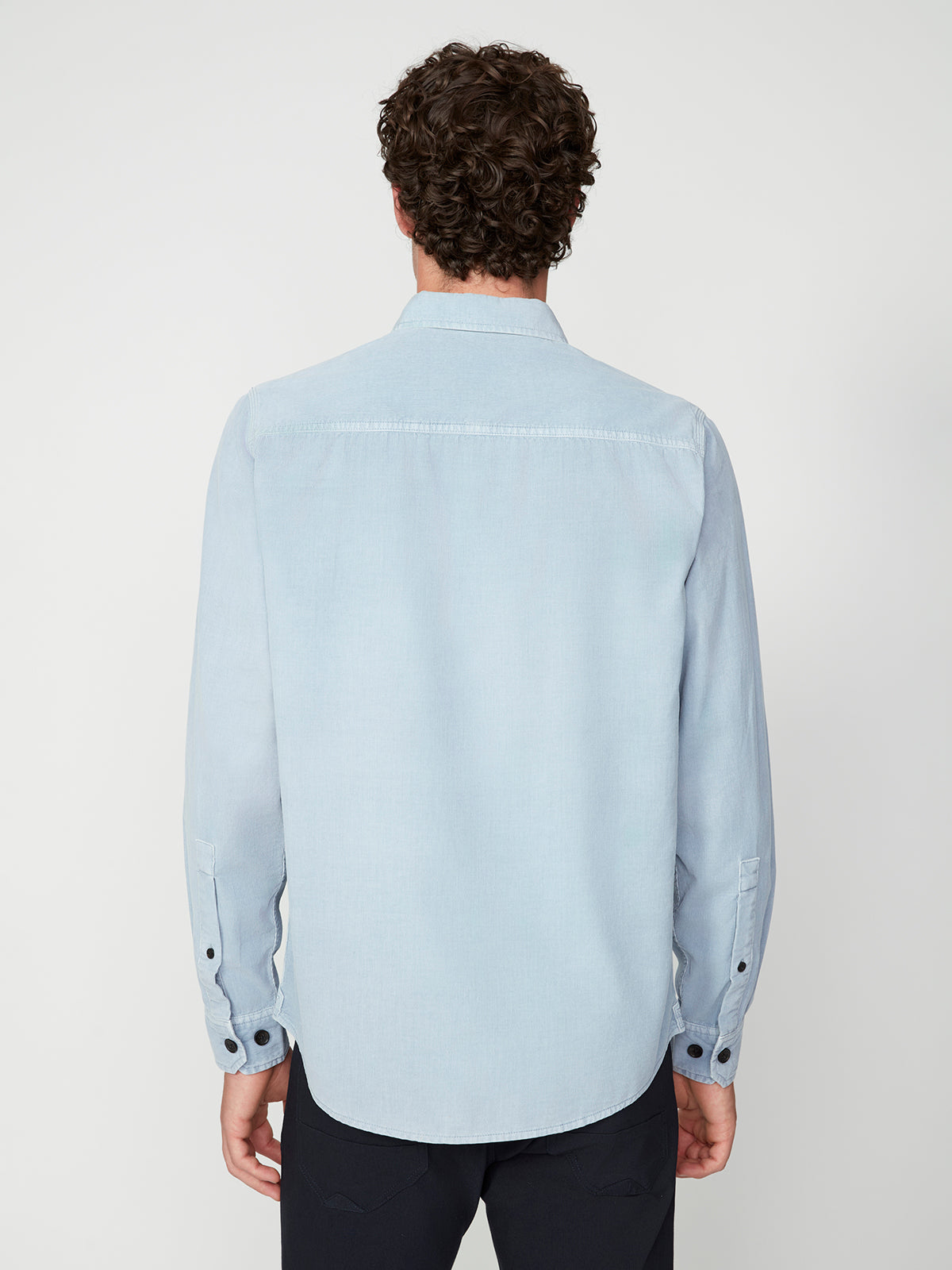 A person with curly hair, seen from behind, is wearing the PROJEK RAW MENS LONG SLEEVES CORDUROY SHIRT in light blue, paired with dark pants against a plain white background.