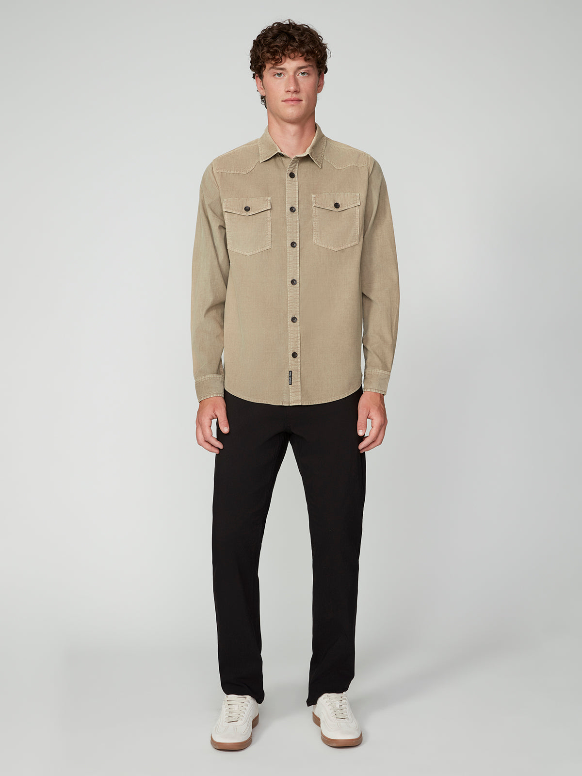 A young man with curly brown hair stands facing forward, wearing a beige PROJEK RAW MENS LONG SLEEVES CORDUROY SHIRT with chest pockets, black pants, and white sneakers against a plain light gray background.