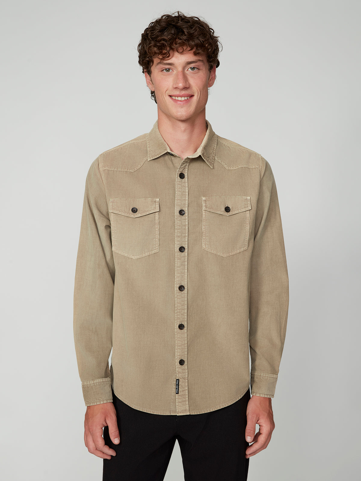 A young man with curly brown hair smiles against a plain light gray background, wearing a PROJEK RAW MENS LONG SLEEVES CORDUROY SHIRT with two chest pockets and black pants.