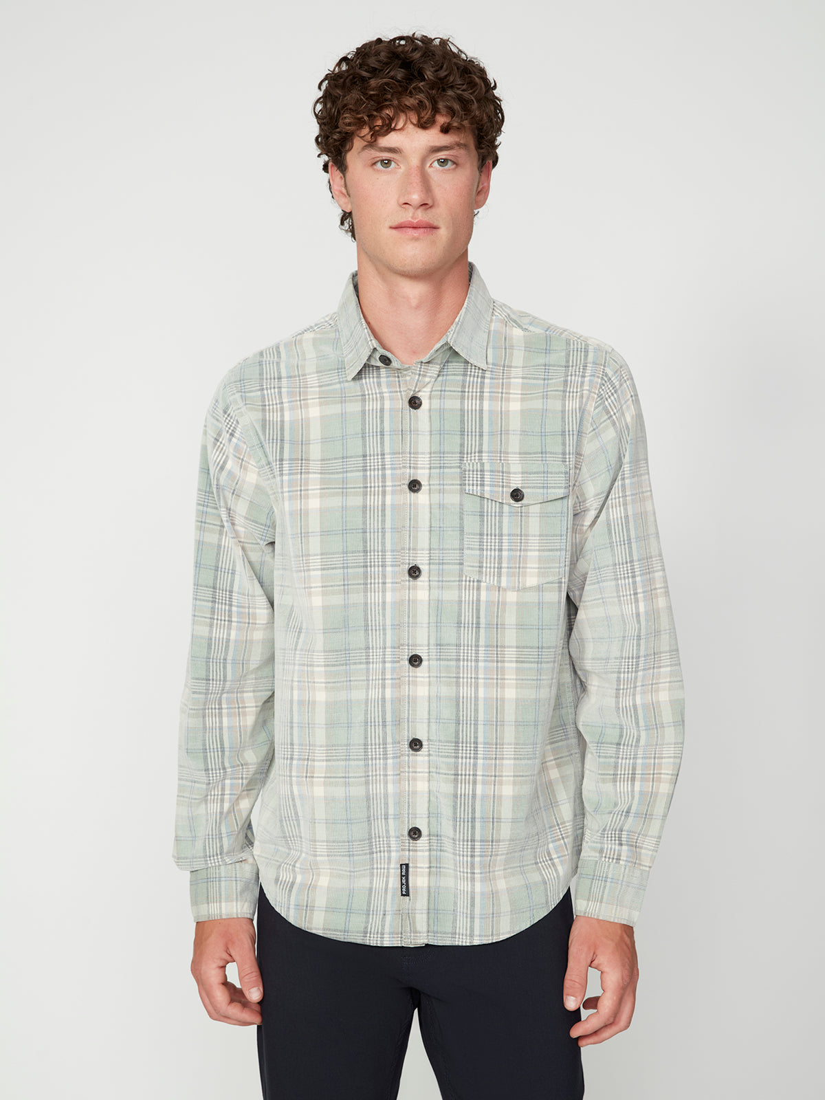 A young man with curly brown hair wears a PROJEK RAW MENS LONG SLEEVES PLAID CORDUROY SHIRT, featuring dark buttons, as he stands against a plain white background.