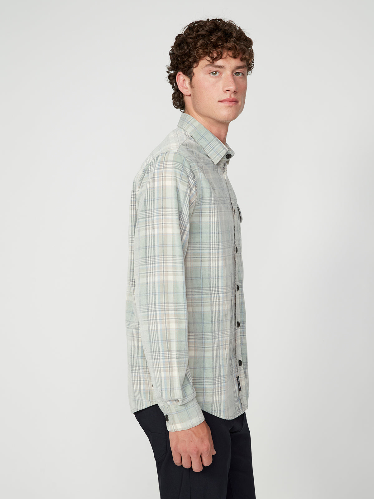 A young man with curly brown hair stands sideways in a PROJEK RAW MENS LONG SLEEVES PLAID CORDUROY SHIRT and dark pants against a plain white background.