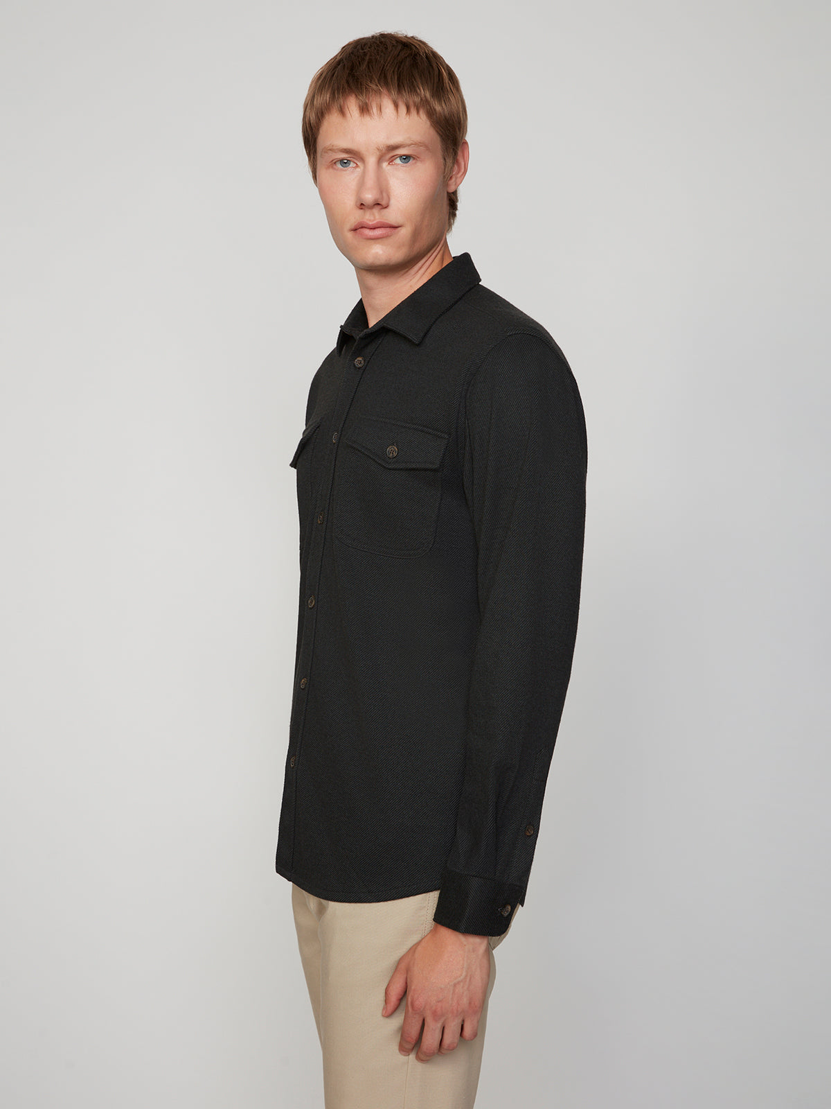 A man with short light brown hair, wearing beige pants and a PROJEK RAW MENS LONG SLEEVES KNIT FLANNEL SHIRT, stands turned slightly to the side against a plain light background.