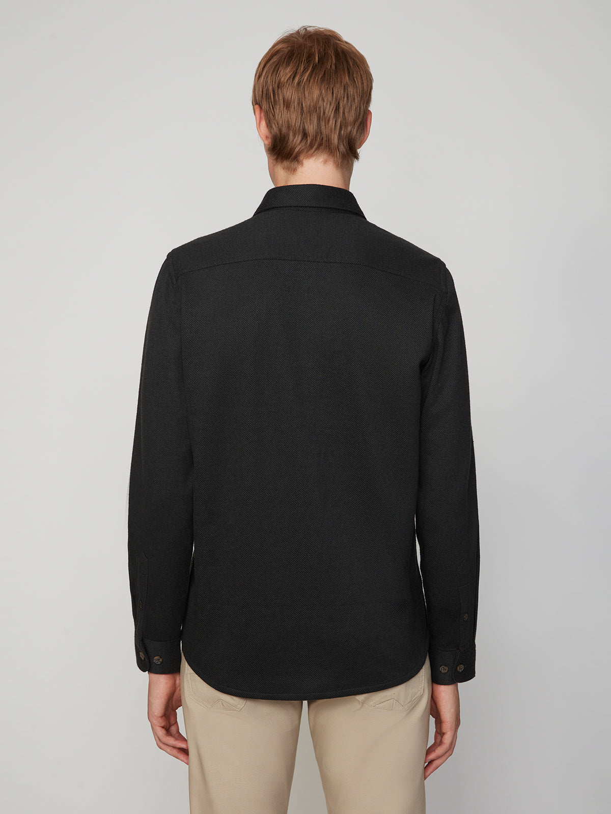 A person with light brown hair is seen from behind wearing a PROJEK RAW MENS LONG SLEEVES KNIT FLANNEL SHIRT in black and beige pants, standing against a plain light background.