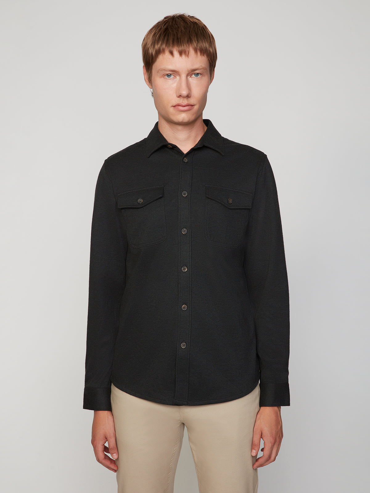 A man with short light brown hair wears a PROJEK RAW MENS LONG SLEEVES KNIT FLANNEL SHIRT with two chest pockets and beige pants, standing against a plain light gray background.