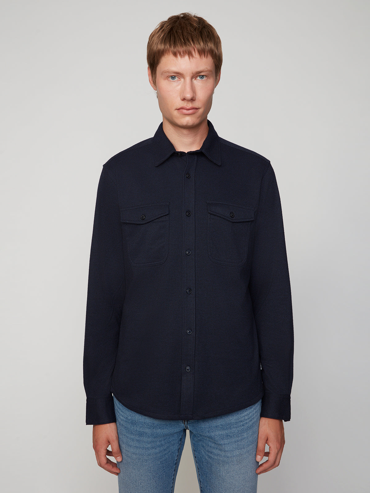 A person with short light brown hair wears a PROJEK RAW MENS LONG SLEEVES KNIT FLANNEL SHIRT in dark navy and light blue jeans, standing against a plain light background and facing the camera.