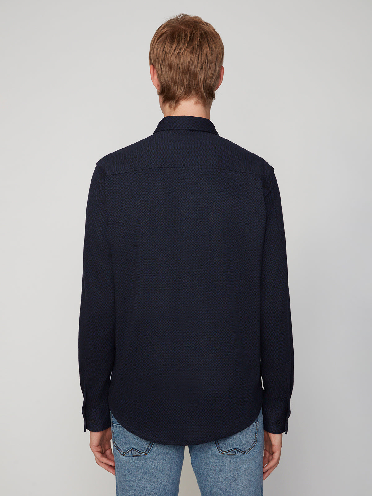 A person with light brown hair stands with their back to the camera, wearing a PROJEK RAW MENS LONG SLEEVES KNIT FLANNEL SHIRT and light blue jeans against a plain light background.