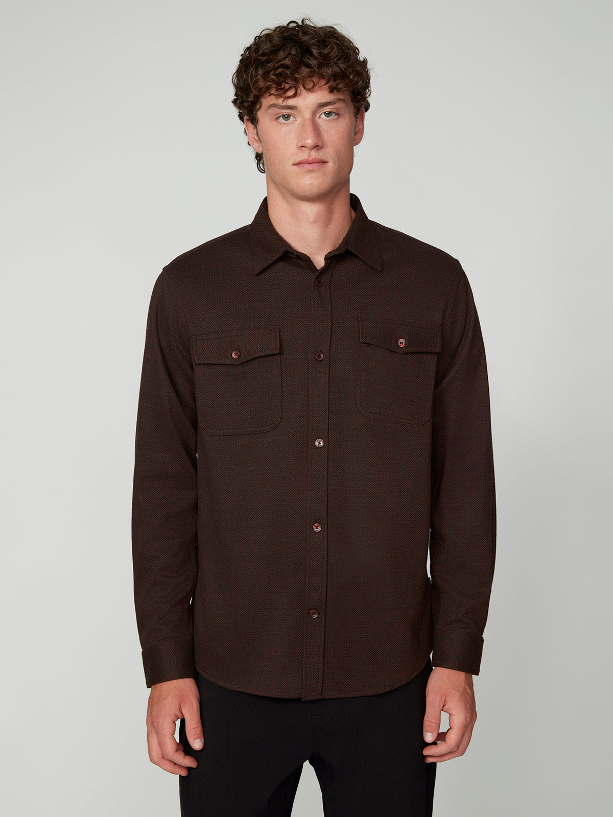 A young man with curly brown hair wears a dark brown PROJEK RAW MENS LONG SLEEVES KNIT FLANNEL SHIRT with two chest pockets, standing against a plain light gray background.