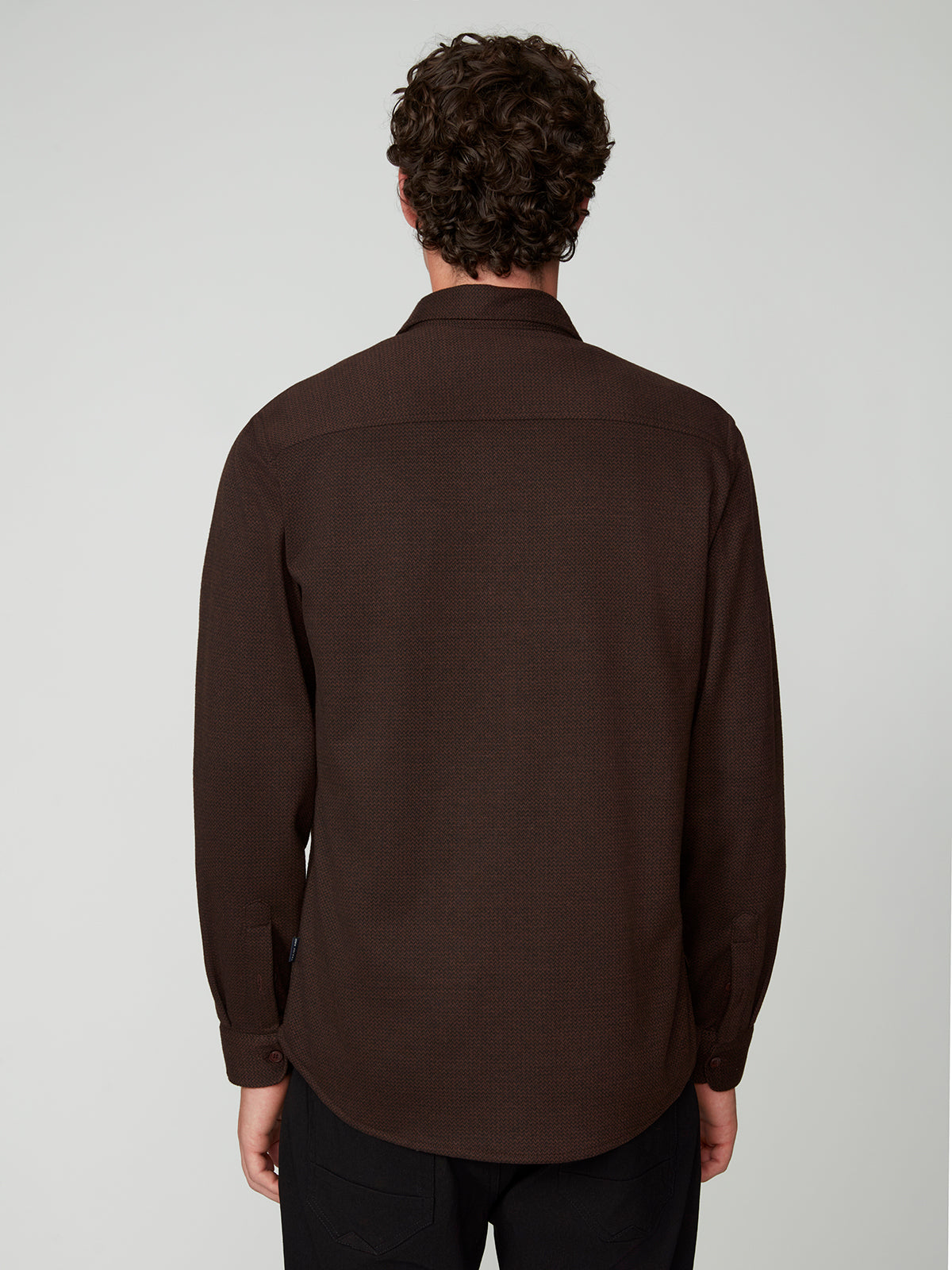 A person with curly hair, seen from behind, wears a PROJEK RAW MENS LONG SLEEVES KNIT FLANNEL SHIRT in dark brown and black pants against a plain light gray background.