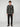 A man with curly hair wears the PROJEK RAW MENS LONG SLEEVE FLANNEL KNIT SHIRT in black and grey plaid, paired with black pants and brown lace-up shoes, standing against a plain light gray background.
