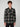 A young man with curly brown hair smiles against a plain background, wearing the PROJEK RAW MENS LONG SLEEVE FLANNEL KNIT SHIRT in black and beige plaid, featuring chest pockets, paired with black pants.