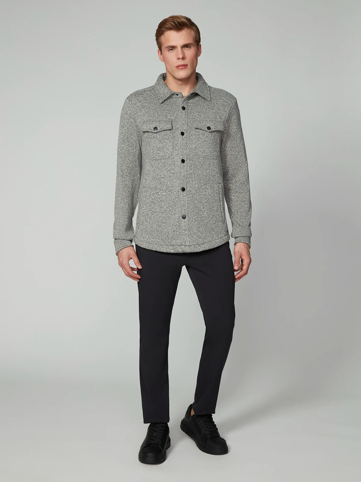 A man with short light brown hair and a neutral expression wears the PROJEK RAW MENS LONG SLEEVE SHERPA LINED OVERSHIRT in light grey, featuring two chest pockets, paired with black pants and black sneakers against a plain background.