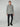 A man with short light brown hair and a neutral expression wears the PROJEK RAW MENS LONG SLEEVE SHERPA LINED OVERSHIRT in light grey, featuring two chest pockets, paired with black pants and black sneakers against a plain background.