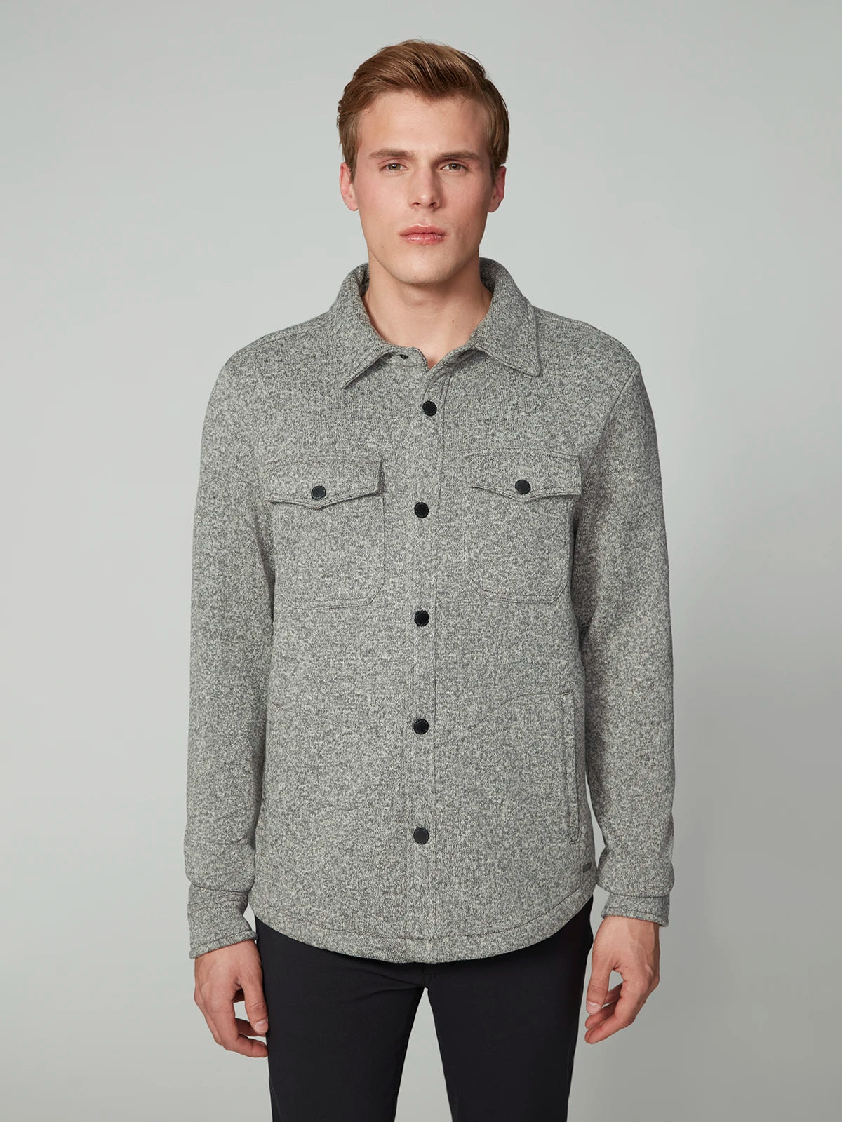 A man with short light brown hair models the PROJEK RAW MENS LONG SLEEVE SHERPA LINED OVERSHIRT, a light gray button-up shirt jacket with front pockets and black buttons, against a plain light gray background.