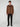 A young man with curly hair wears the PROJEK RAW MENS LONG SLEEVE FAUX SUEDE OVERSHIRT in brown over a black shirt, pants, and boots. Set against a light gray background, this piece is a perfect lightweight layer for any season.