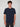 A young man with curly brown hair wears the PROJEK RAW MENS SHORT SLEEVE CREW NECK T-SHIRT in navy blue and dark pants, standing facing the camera against a light grey background—ideal for any casual wardrobe.