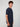 A young man with curly brown hair stands sideways, wearing a PROJEK RAW MENS SHORT SLEEVE CREW NECK T-SHIRT in navy and dark pants against a light gray background.