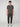 A young man with curly hair faces forward, wearing a PROJEK RAW MENS SHORT SLEEVE CREW NECK T-SHIRT in dark gray, dark jogger pants with side pockets, and white sneakers—creating a perfect casual look against a plain light background.