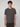 A young man with short curly hair models the PROJEK RAW MENS SHORT SLEEVE CREW NECK T-SHIRT in dark gray, paired with black pants against a light gray background—an essential piece for any casual wardrobe.