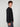A young man with curly brown hair stands sideways, looking at the camera against a plain white background, wearing a PROJEK RAW 147333 BLACK long-sleeve shirt and gray pants.
