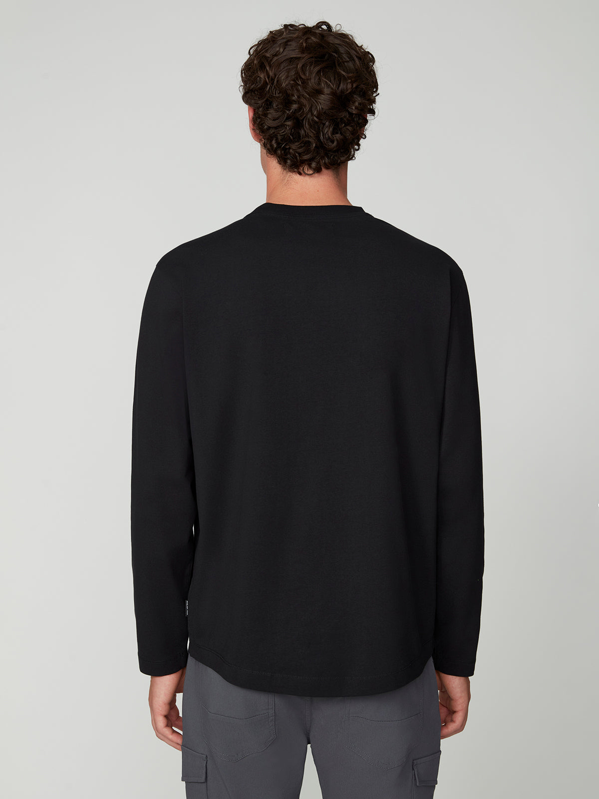 A person with curly brown hair is shown from the back, wearing PROJEK RAW 147333 BLACK long-sleeved shirt and gray cargo pants, standing against a plain light gray background.