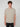 A young man with curly brown hair wears the PROJEK RAW MENS SHORT SLEEVE CREW NECK T-SHIRT in beige and black pants, standing against a light gray background—a versatile casual staple.