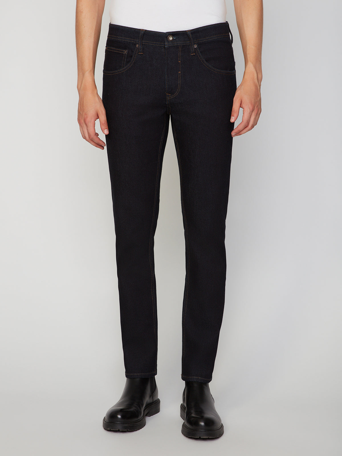 A person wears PROJEK RAW MENS STRETCH SLIM FIT JEAN with a white shirt and black boots, standing against a plain light background. The modern slim silhouette is showcased in this cropped, shoulder-down image.