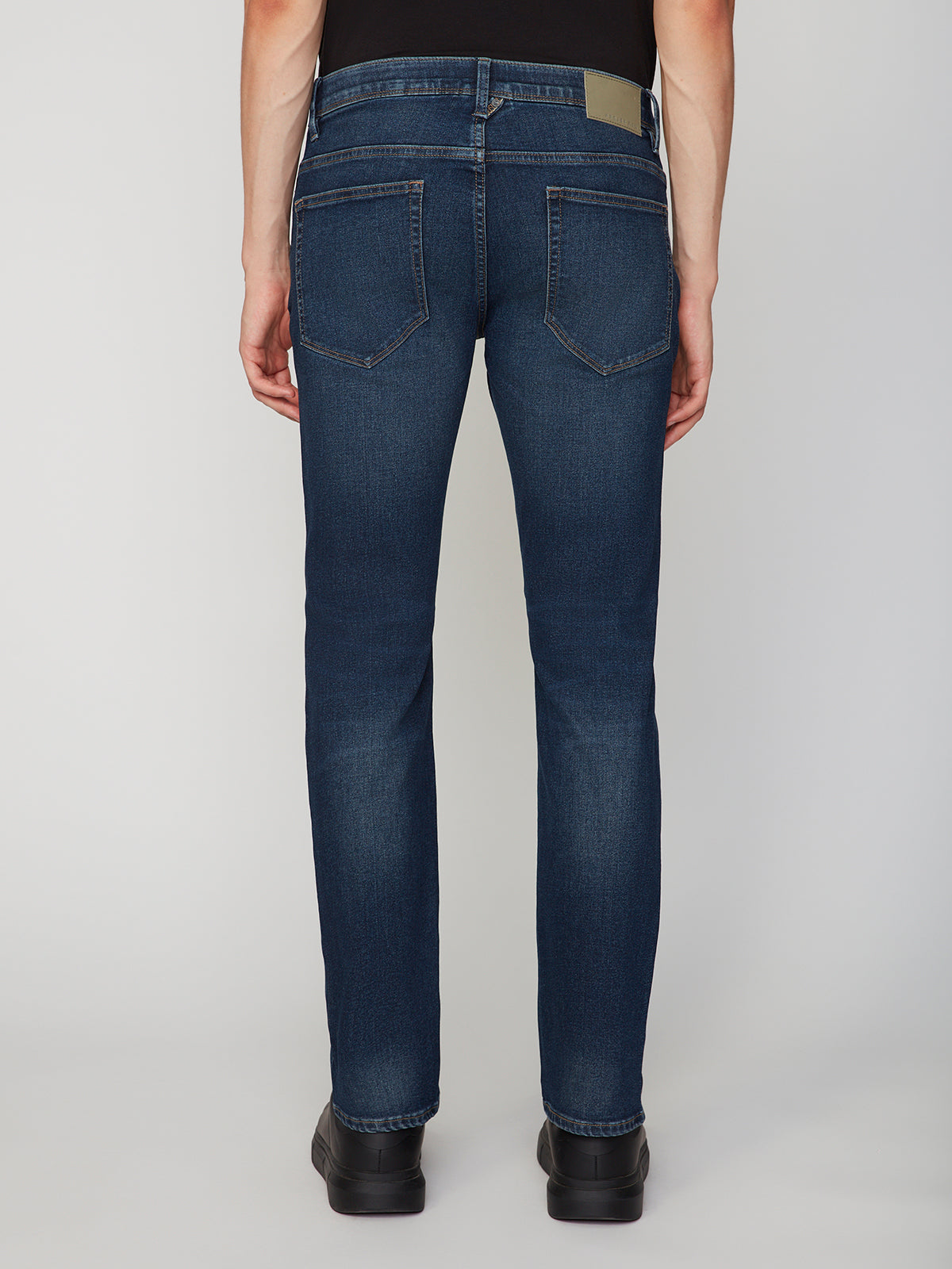 A person models PROJEK RAW MENS BARU STRAIGHT FIT JEAN in dark blue stretch slub denim with black shoes, shown from the back against a plain light background.